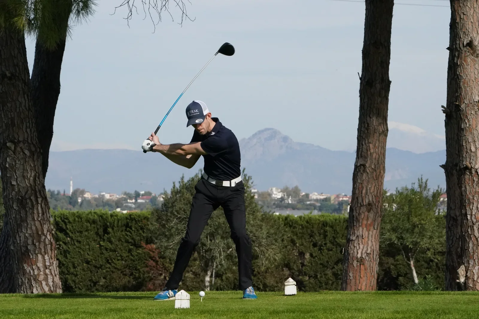 A golfer making a driver swing from a tee between two trees